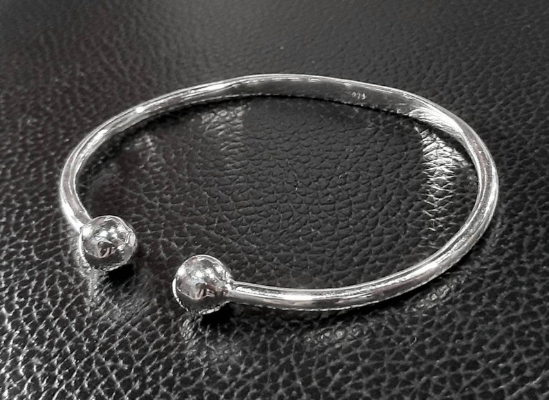 Op de afbeelding: Een zilveren armband met twee ronde, gladde uiteinden. De armband is open en heeft een eenvoudig, minimalistisch ontwerp.