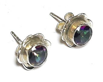 May include: A pair of silver-toned stud earrings. Each earring features a round, iridescent gemstone set within a flower-shaped bezel. The gemstones display a mix of colors, including purple, green, and blue. The earrings are set against a white background.