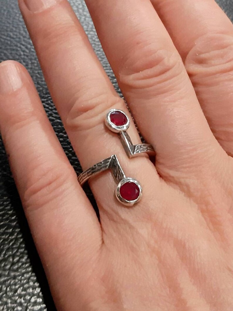 Op de afbeelding: Een zilveren ring met twee rode edelstenen. De ring heeft een geometrisch ontwerp met een getextureerde band.