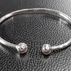 Op de afbeelding: Een zilveren armband met twee ronde, getextureerde uiteinden.