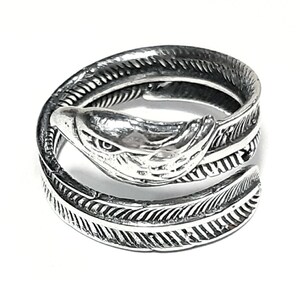 May include: A silver-colored ring in the shape of a snake with feather-like detailing. The snake's head is at the top, with detailed eyes and scales. The ring wraps around the finger, creating a unique and stylish accessory.