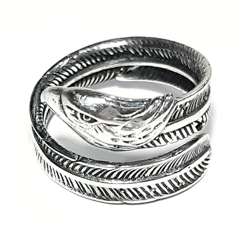 May include: A silver-colored ring in the shape of a snake with feather-like detailing. The snake's head is at the top, with detailed eyes and scales. The ring wraps around the finger, creating a unique and stylish accessory.
