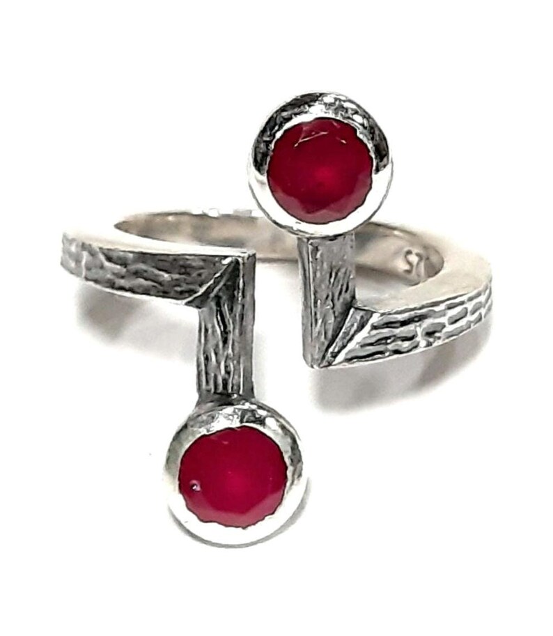 Op de afbeelding: Een zilveren ring met een getextureerde band en twee rode edelstenen. De ring is aan &eacute;&eacute;n kant open en heeft een uniek ontwerp.