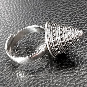 May include: A silver ring with a cone-shaped top. The cone is made of multiple bands of silver, each with a row of small beads.