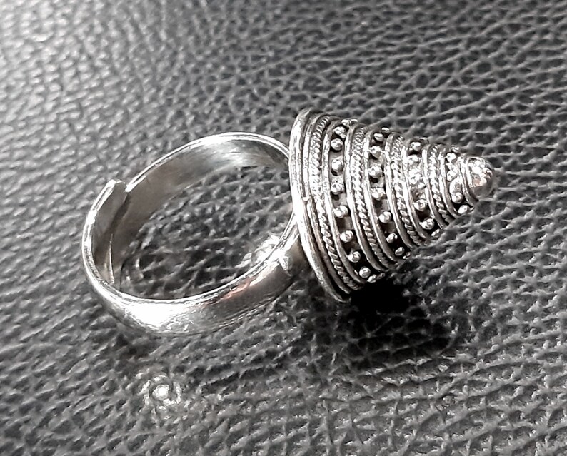 May include: A silver ring with a cone-shaped top. The cone is made of multiple bands of silver, each with a row of small beads.