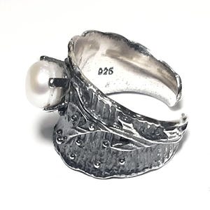 May include: A silver ring with a pearl set in a leaf design. The ring is marked with the number "925" on the inside.