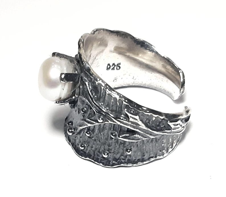 May include: A silver ring with a pearl set in a leaf design. The ring is marked with the number "925" on the inside.