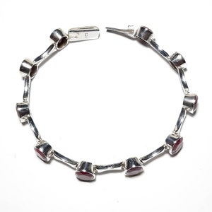 May include: A silver bracelet with red gemstones. The bracelet has a clasp closure and is made of sterling silver.