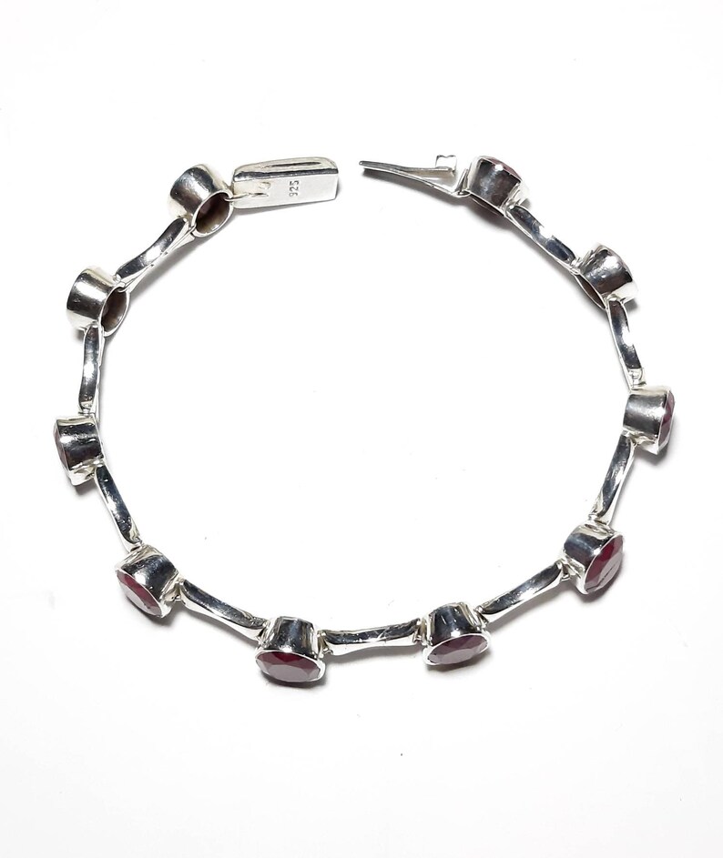 May include: A silver bracelet with red gemstones. The bracelet has a clasp closure and is made of sterling silver.