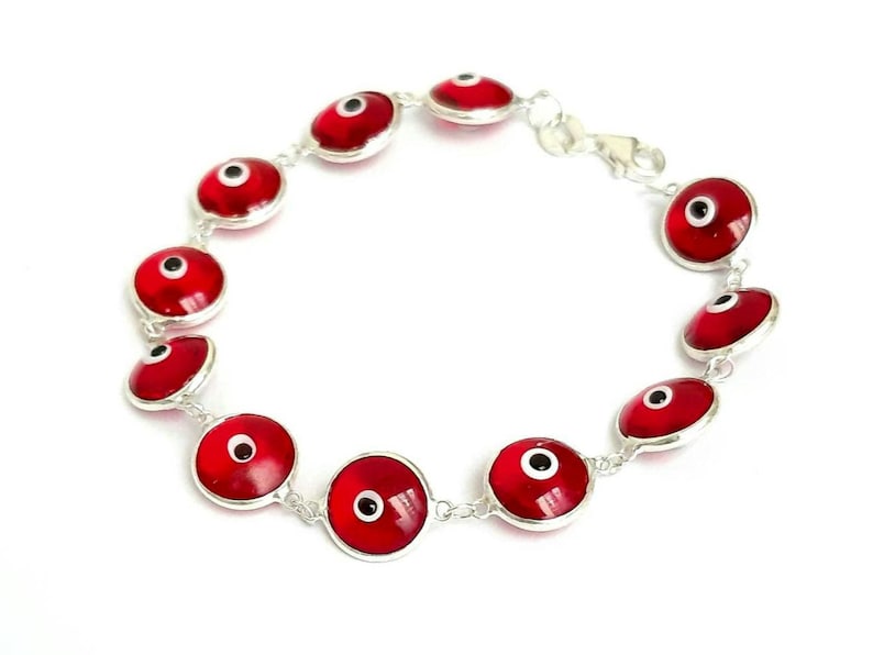 May include: A silver bracelet with red evil eye charms. The charms are round and have a white eye with a black pupil.