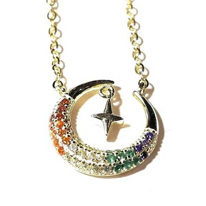 May include: A gold chain necklace with a crescent moon pendant. The moon is decorated with colorful gemstones and a small star charm hangs from the center.