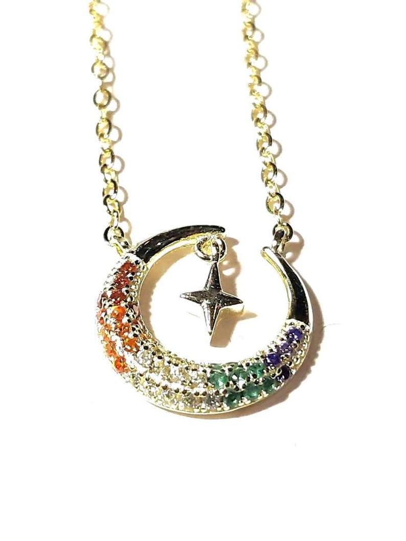 May include: A gold chain necklace with a crescent moon pendant. The moon is decorated with colorful gemstones and a small star charm hangs from the center.