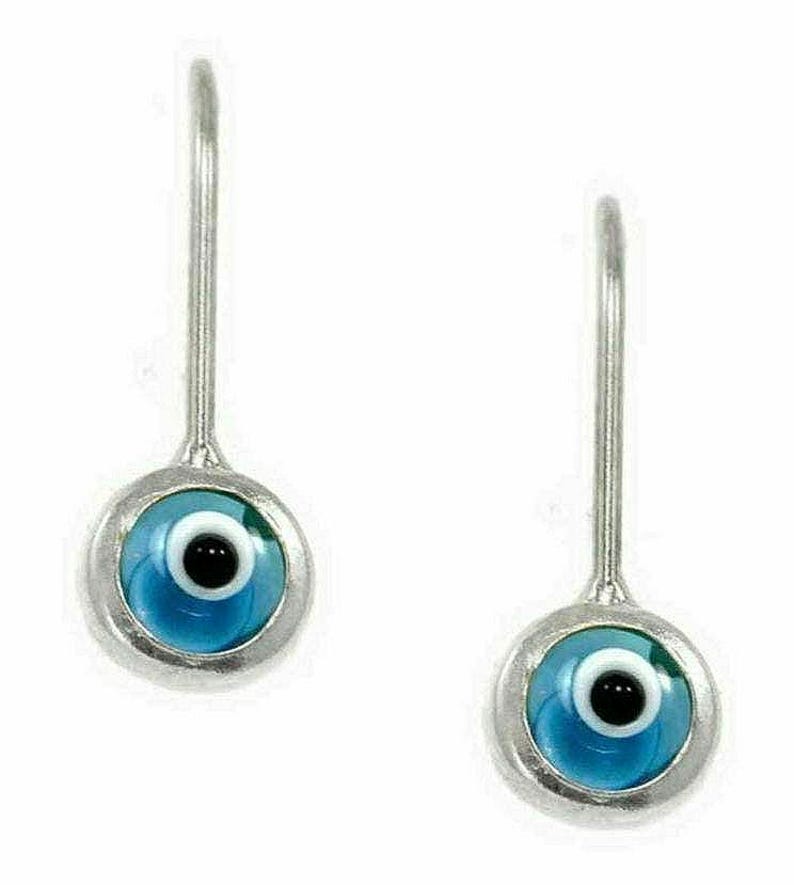 K&ouml;nnte beinhalten: Ein Paar silberne Ohrringe mit blauen b&ouml;sen Augen-Anh&auml;ngern. Die Anh&auml;nger sind rund und haben eine wei&szlig;e Mitte mit einer schwarzen Pupille.