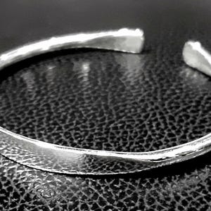 May include: A silver bangle bracelet with a hammered finish. The bracelet is open and has a simple, minimalist design.