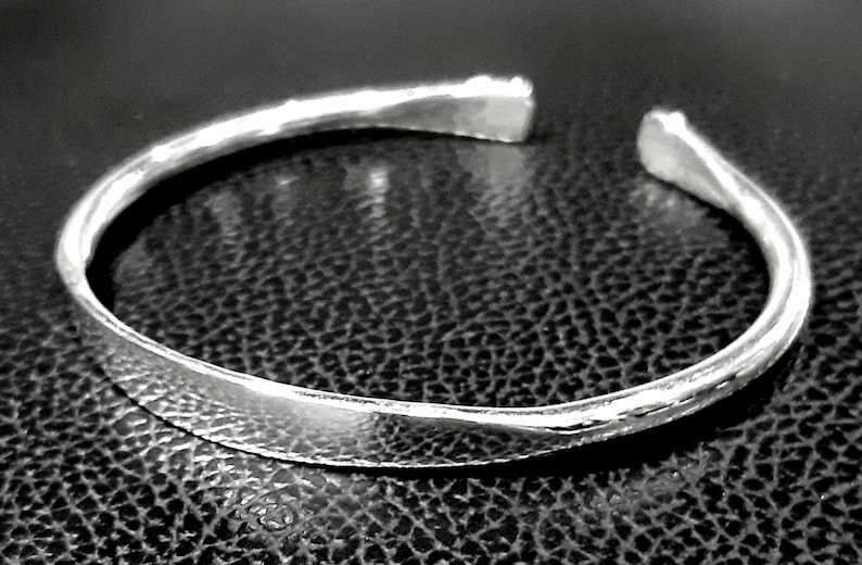 May include: A silver bangle bracelet with a hammered finish. The bracelet is open and has a simple, minimalist design.