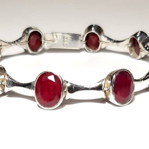 May include: A silver bracelet with red oval gemstones. The bracelet has a hinged clasp.
