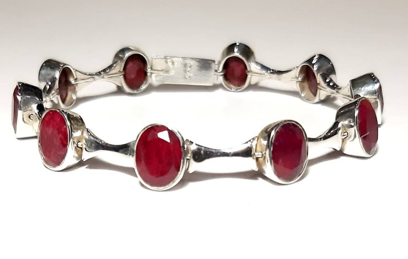 May include: A silver bracelet with red oval gemstones. The bracelet has a hinged clasp.