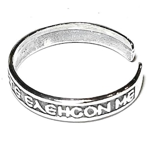 May include: A silver-colored adjustable ring with the inscription "ELEHCON ME" in capital letters. The ring is open-ended and sits on a white background. The ring is likely made of sterling silver.