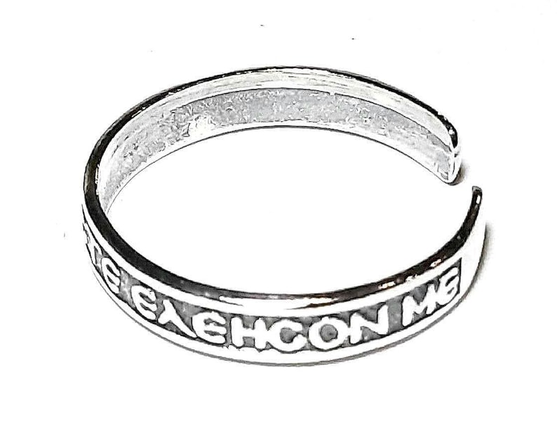 May include: A silver-colored adjustable ring with the inscription "ELEHCON ME" in capital letters. The ring is open-ended and sits on a white background. The ring is likely made of sterling silver.