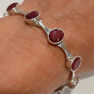 May include: A silver bangle bracelet with five red gemstone accents. The bracelet is open and has a curved design.
