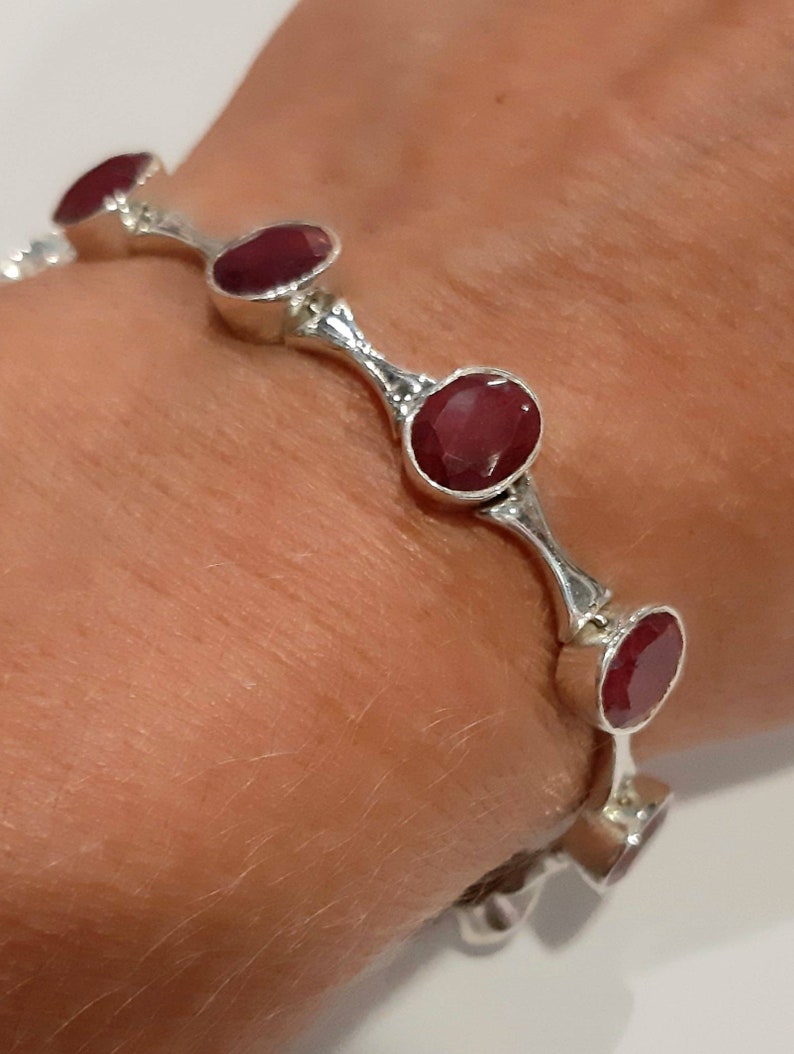 May include: A silver bangle bracelet with five red gemstone accents. The bracelet is open and has a curved design.