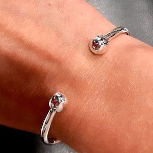 Könnte beinhalten: Zwei silberne Armreifen mit einer runden Kugel an jedem Ende. Die Armreifen befinden sich am Handgelenk einer Person.