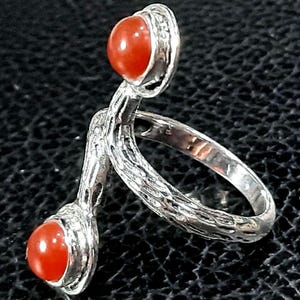 May include: A silver ring with two orange carnelian stones. The ring has a textured, twisted band.