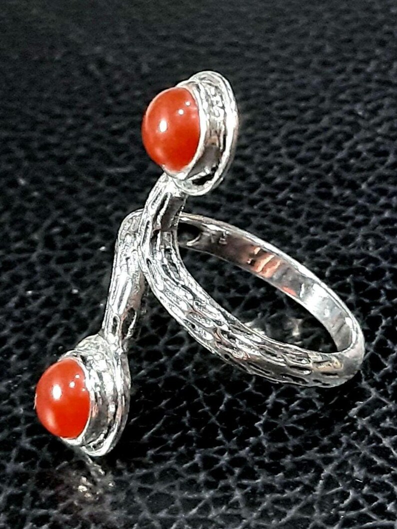 May include: A silver ring with two orange carnelian stones. The ring has a textured, twisted band.