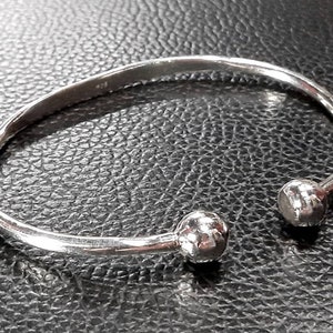 Op de afbeelding: Een zilveren armband met twee ronde, getextureerde uiteinden.