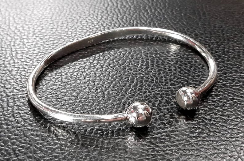 Op de afbeelding: Een zilveren armband met twee ronde, getextureerde uiteinden.