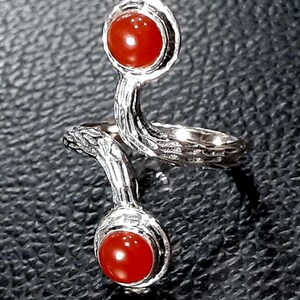 May include: A silver ring with two red carnelian stones. The ring is designed with a twisted band and the stones are set in a bezel setting.