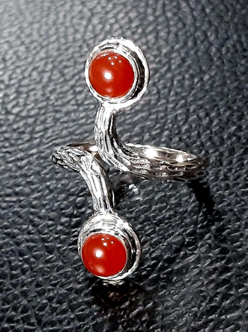 May include: A silver ring with two red carnelian stones. The ring is designed with a twisted band and the stones are set in a bezel setting.