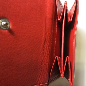 May include: A red leather wallet with multiple folds and a snap closure. The wallet is open to reveal the interior.