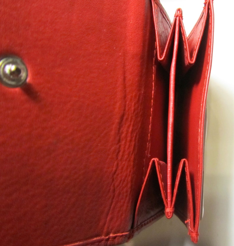 May include: A red leather wallet with multiple folds and a snap closure. The wallet is open to reveal the interior.