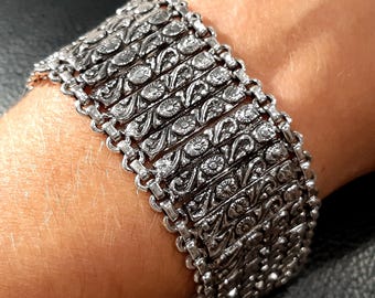 May include: A silver bracelet with a detailed floral design. The bracelet is made of multiple linked chains with intricate patterns.