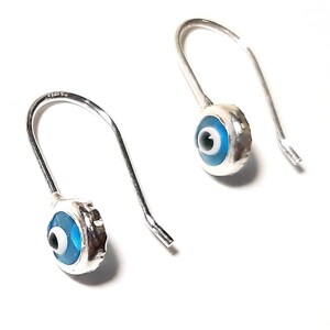K&ouml;nnte beinhalten: Ein Paar silberne Ohrringe mit blauen b&ouml;sen Augen-Anh&auml;ngern. Die Ohrringe sind aus Sterlingsilber gefertigt und haben ein schlichtes Haken-Design.