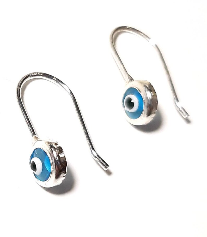 K&ouml;nnte beinhalten: Ein Paar silberne Ohrringe mit blauen b&ouml;sen Augen-Anh&auml;ngern. Die Ohrringe sind aus Sterlingsilber gefertigt und haben ein schlichtes Haken-Design.
