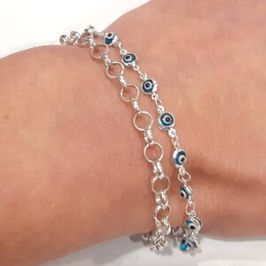 Puede incluir: Un brazalete de cadena de plata con m&uacute;ltiples hebras de peque&ntilde;os c&iacute;rculos de plata y abalorios de ojo azul.