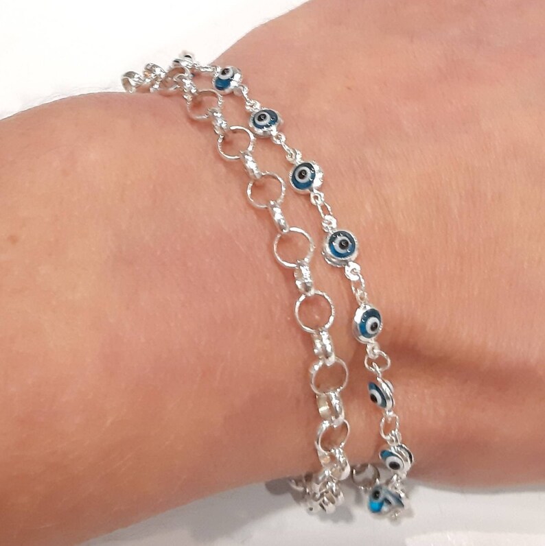 Puede incluir: Un brazalete de cadena de plata con m&uacute;ltiples hebras de peque&ntilde;os c&iacute;rculos de plata y abalorios de ojo azul.