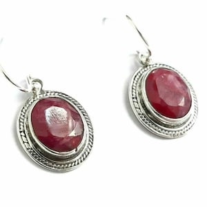 May include: A pair of silver earrings with red ruby gemstones. The earrings have a simple design with a round, bezel-set stone.