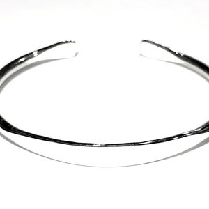 May include: A silver bangle bracelet with a smooth, rounded surface.