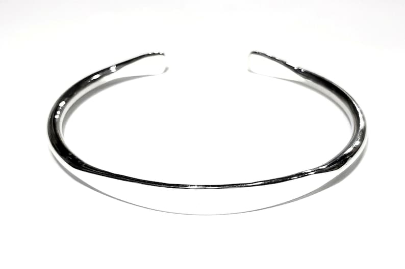 May include: A silver bangle bracelet with a smooth, rounded surface.