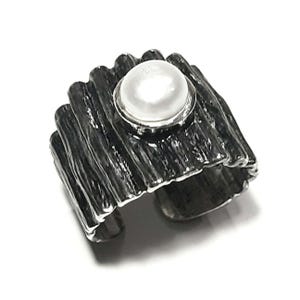 May include: A silver ring with a textured, wood-like band and a white pearl set in a silver bezel.