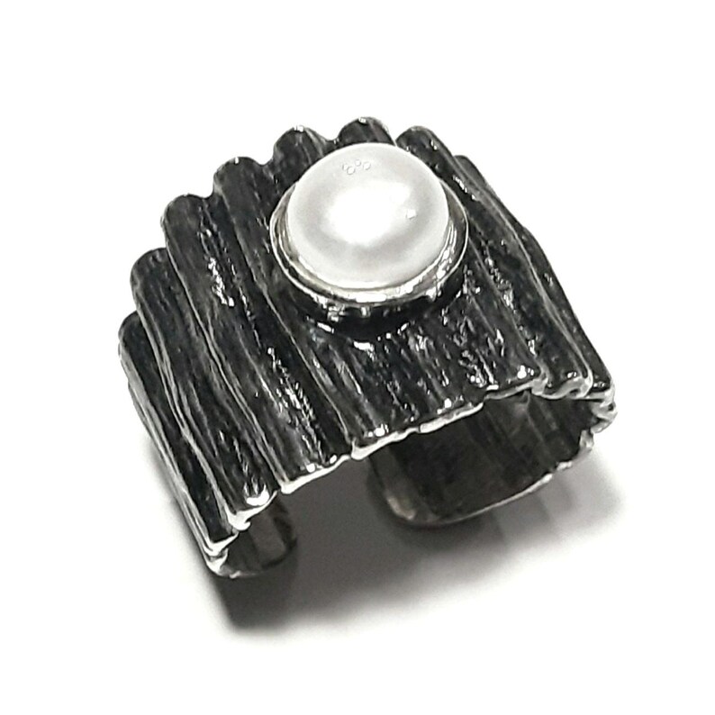 May include: A silver ring with a textured, wood-like band and a white pearl set in a silver bezel.
