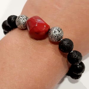 Puede incluir: Un brazalete con cuentas de roca de lava negra, cuentas plateadas y una cuenta de coral rojo.