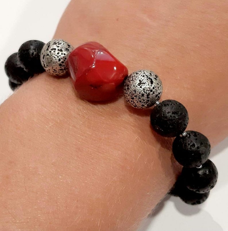 Puede incluir: Un brazalete con cuentas de roca de lava negra, cuentas plateadas y una cuenta de coral rojo.