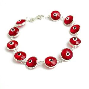 May include: A silver bracelet with red evil eye charms. The charms are round and have a white eye with a black pupil.