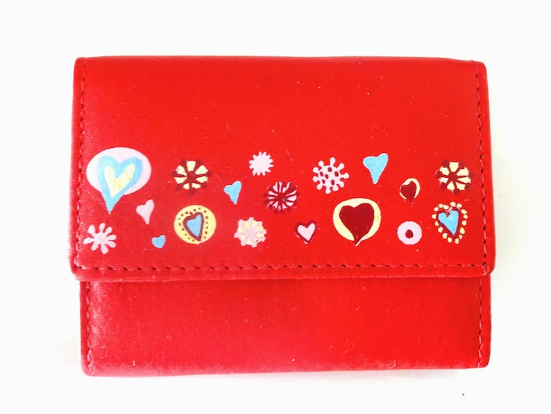 May include: A red leather wallet with a colorful design of hearts, flowers, and circles. The design is hand-painted and features a variety of colors, including pink, blue, yellow, and green.