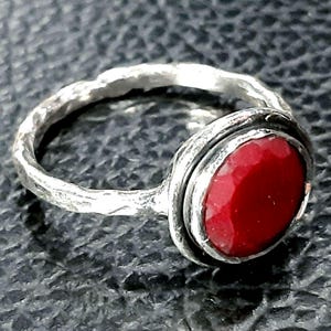 Pu&ograve; includere: Un anello d'argento con una fascia testurizzata e una pietra preziosa rossa incastonata in una montatura a castone.