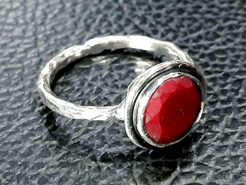 Pu&ograve; includere: Un anello d'argento con una fascia testurizzata e una pietra preziosa rossa incastonata in una montatura a castone.
